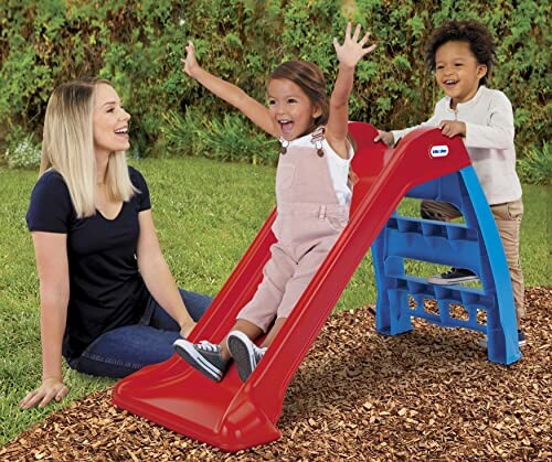 Two children playing on a red slide with a woman sitting nearby.